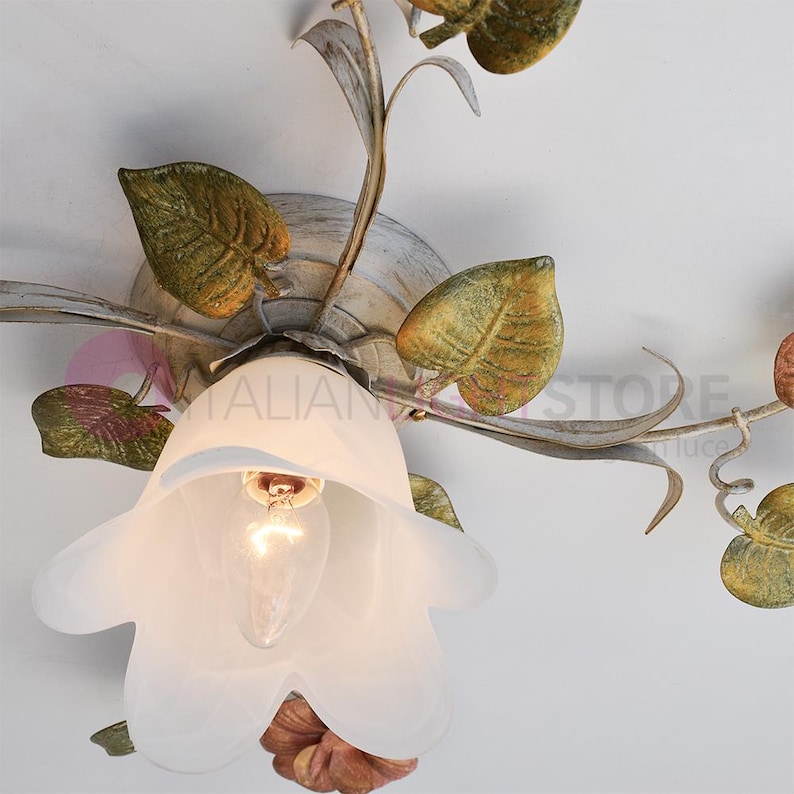 K&ouml;nnte beinhalten: Eine wei&szlig;e Deckenleuchte mit floralem Design. Die Leuchte hat einen wei&szlig;en, mattierten Glasschirm in Form einer Blume. Die Bl&auml;tter sind in Gr&uuml;n- und Braunt&ouml;nen bemalt.