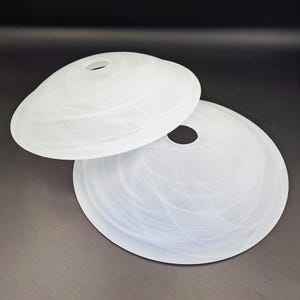 Può includere: Due paralumi bianchi in vetro smerigliato. Ogni paralume ha una forma a ciotola poco profonda e arrotondata con un foro circolare nella parte superiore. Il vetro presenta un sottile motivo a spirale. Per lampade da soffitto.