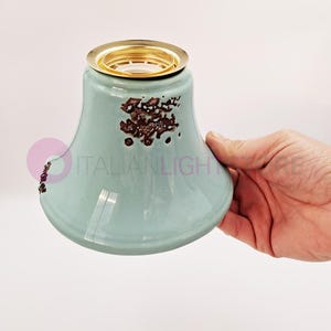 Peut inclure: Un abat-jour de lampe en céramique bleu clair avec une bordure en métal doré et des mouchetures brunes. L'abat-jour est tenu dans une main.