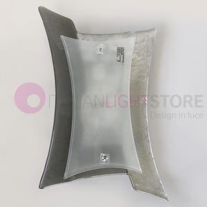 Puede incluir: Una lámpara de pared moderna con una pantalla de vidrio esmerilado y un marco de metal plateado. La lámpara tiene un diseño curvo único y es perfecta para agregar un toque de elegancia a cualquier habitación.