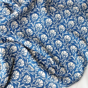 May include: A close-up of a blue and white floral fabric. The fabric displays a repeating pattern of stylized white flowers and leaves against a deep blue background. The fabric is draped, showing folds and texture.