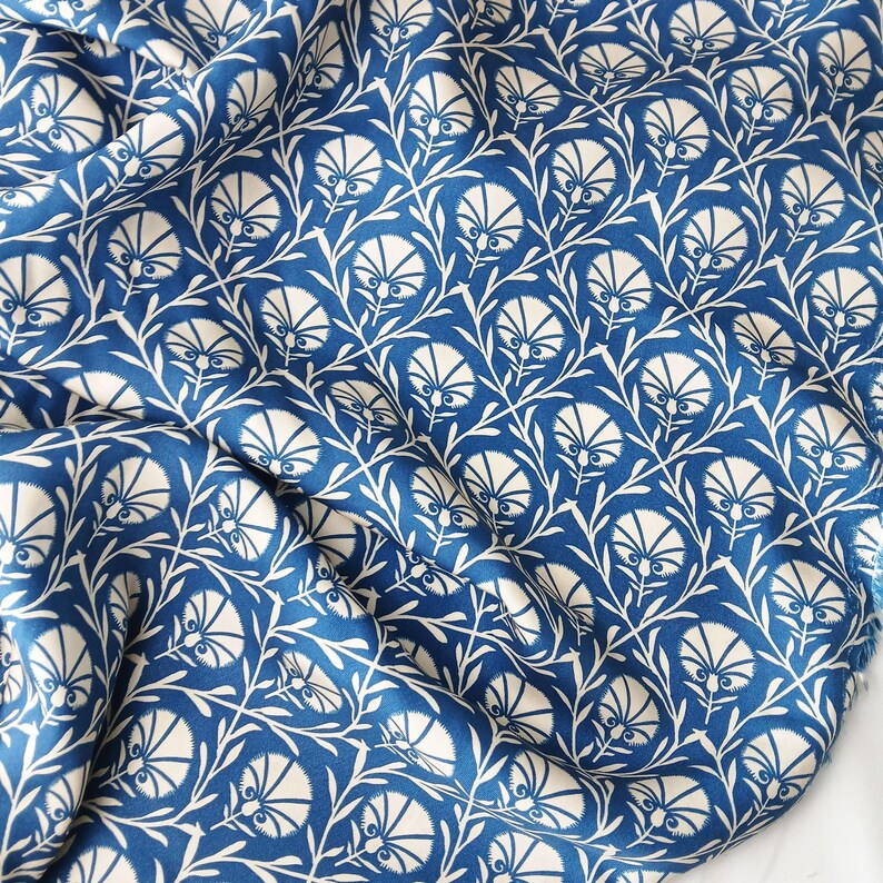 May include: A close-up of a blue and white floral fabric. The fabric displays a repeating pattern of stylized white flowers and leaves against a deep blue background. The fabric is draped, showing folds and texture.