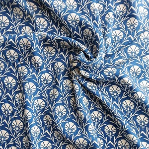 May include: A close-up of blue fabric with a white floral pattern. The design features stylized white flowers and leaves against a deep blue background. The fabric is draped, showing folds and texture.