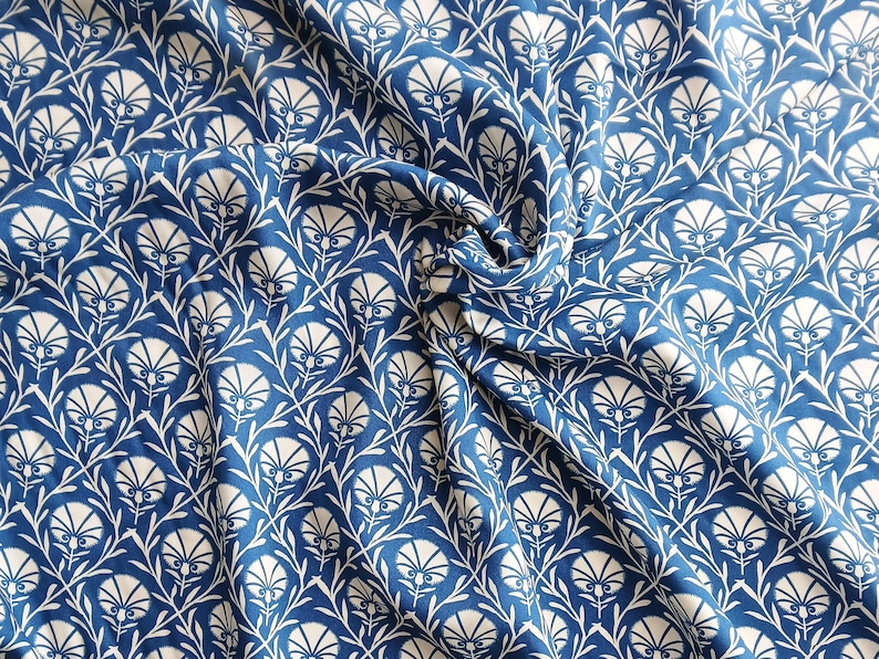 May include: A close-up of blue fabric with a white floral pattern. The design features stylized white flowers and leaves against a deep blue background. The fabric is draped, showing folds and texture.