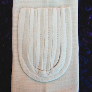 May include: A beige knee support with a padded, ribbed inner lining. The support has a white trim around the edges.
