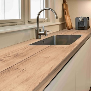 May include: A kitchen sink area featuring a stainless steel faucet with a curved neck, a rectangular stainless steel basin, and a light brown wood-grain countertop. A dark gray coffee machine and two wooden cutting boards sit nearby.