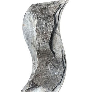 May include: A vertical, S-shaped sculpture featuring a rough, textured surface with natural gray and charcoal stone-like patterns. The object has a curved, wave-like silhouette with sharp, defined edges and a flat base for stable placement.