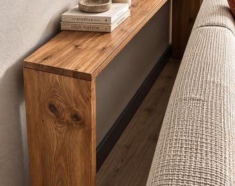 Può includere: Un tavolo console lungo e stretto realizzato in legno naturale con venature e nodi visibili. Il tavolo presenta un piano rettangolare piatto e due pannelli laterali verticali, che sostengono una pila di libri, una ciotola in pietra e una candela.