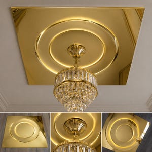 May include: A square, reflective gold ceiling panel featuring a central circular recessed design with integrated LED lighting. A tiered, cylindrical crystal chandelier with a gold-toned metal frame hangs from the centre of the panel.