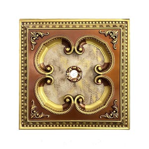 May include: A square decorative ceiling medallion featuring a bronze and gold finish. The center has a textured beige marble-like inlay with a small circular floral motif. The frame is adorned with intricate scrollwork and a beaded border edge.