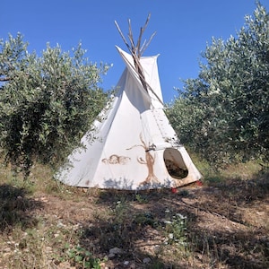 May include: A white teepee tent with a wooden frame, set up outdoors in a field with green trees and a blue sky.