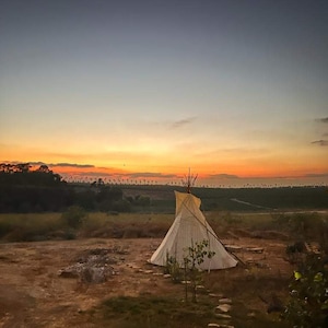 May include: A white teepee tent sits on a dirt path in a field with a sunset in the background.