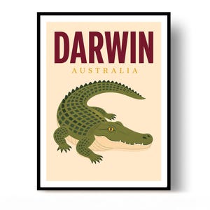 May include: A framed wall art print featuring a green crocodile illustration on a light cream background. The text DARWIN is printed in large dark red letters above the word AUSTRALIA in smaller gold letters. The crocodile has yellow eyes.
