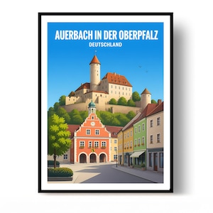 May include: A framed travel poster featuring the text AUERBACH IN DER OBERPFALZ DEUTSCHLAND. The illustration depicts a town square with a red building, colorful houses, and a large castle on a hill under a clear blue sky with two birds.