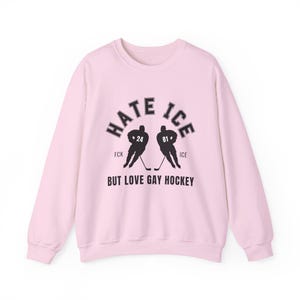 May include: A light pink sweatshirt with the text "HATE ICE" above two hockey player silhouettes and the text "BUT LOVE GAY HOCKEY" below. The hockey players are black and have the numbers 24 and 81 on their jerseys.