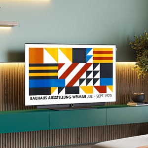 May include: A modern living room with a flat screen TV displaying a geometric design with the text "BAUHAUS AUSSTELLUNG WEIMAR JULI - SEPT 1923". The TV is mounted on a dark green shelf with two drawers. The wall behind the TV is a light green color with a wood paneling.