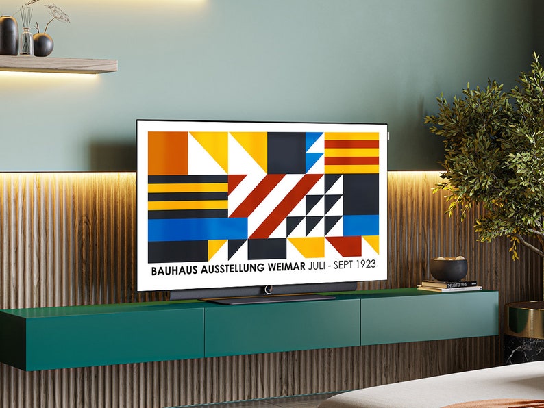 May include: A modern living room with a flat screen TV displaying a geometric design with the text "BAUHAUS AUSSTELLUNG WEIMAR JULI - SEPT 1923". The TV is mounted on a dark green shelf with two drawers. The wall behind the TV is a light green color with a wood paneling.