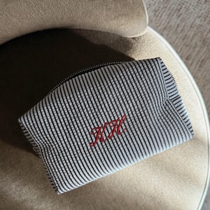 Peut inclure: Une trousse de toilette rayée noire et blanche avec un monogramme brodé rouge "K.H."