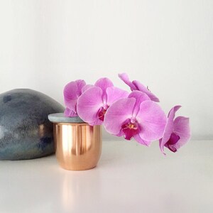 Könnte beinhalten: Ein Kupferbehälter mit einem grauen Deckel, der einen Strauß rosa Orchideen enthält.