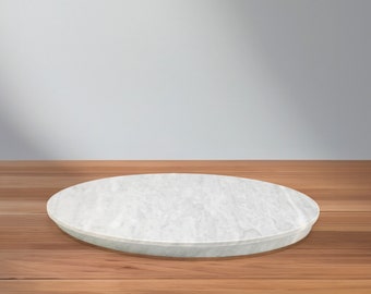 Puede incluir: Un pedestal redondo de mármol blanco sobre una superficie de madera. El pedestal es liso y de color gris claro.