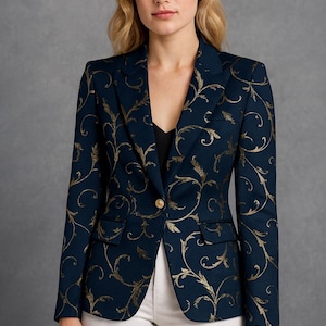 May include: Navy blue blazer with gold floral pattern. The blazer has a single-button closure and two front pockets. The gold pattern is a swirling, ornate design. The blazer is worn with white pants and a black top.