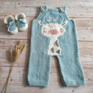 Op de afbeelding: Een lichtblauwe gebreide baby romper met een giraffenprint. De romper heeft een knoopsluiting op de schouders en een schattig giraffen gezicht op de voorkant.