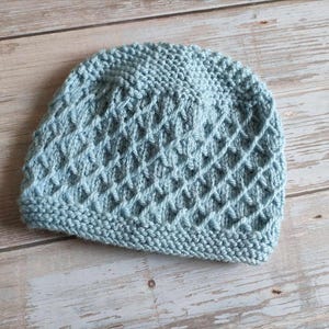Puede incluir: Un gorro de punto azul claro con un patrón de rombos texturizado.