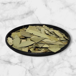 May include: A black bowl filled with dried bay leaves. The leaves are a light brown color and have a slightly green tint.