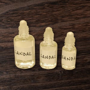 Small glass bottle of sandal attar in 3ml, 6ml, and 12ml sizes with roll-on applicator