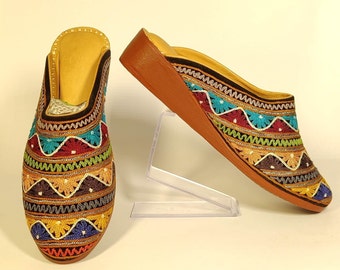 May include: A pair of colourful embroidered slippers with a wedge heel. The slippers have a brown leather sole and are decorated with a variety of colourful threads in a geometric pattern.