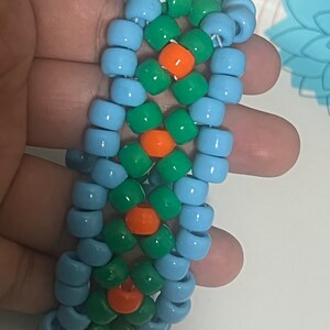 May include: A blue, green, and orange beaded bracelet. The bracelet is made with small, round beads that are strung together in a pattern.