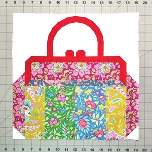 Puede incluir: Un bolso de tela patchwork con un asa roja. El bolso está hecho de tela floral en tonos de rosa, verde, azul y amarillo.