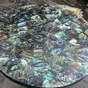 Könnte beinhalten: Eine runde Tischplatte aus einem Mosaik aus schillernden Abalone-Muschelschalentilen. Die Fliesen sind in einem geometrischen Muster angeordnet und haben eine Vielzahl von Farben, darunter Grün, Blau und Lila.