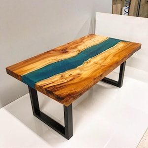 May include: A wooden coffee table with a blue epoxy river running through the centre. The table has black metal legs.
