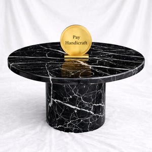 May include: A black marble side table with white veining. The table has a round top and a cylindrical base. A gold-colored disc with the text "Pay Handicraft" is on top of the table.