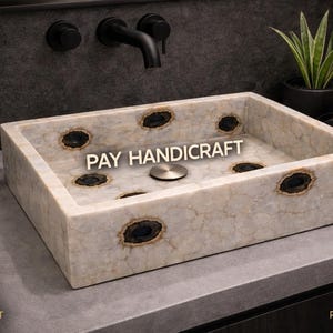 Könnte beinhalten: Rechteckiges Waschbecken aus Marmor mit dunklen Akzenten. Das Waschbecken hat ein helles Stein-Aussehen mit dunklen, oval geformten Einlagen. Der Text "PAY HANDICRAFT" ist auf dem Waschbecken zu sehen. Ein schwarzer Wasserhahn und Zubehör sind im Hintergrund sichtbar.