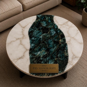May include: A round coffee table featuring a white marble surface with a central, irregular band of dark teal and black veined stone. A rectangular brass-colored plaque is centered on the table, displaying the text PAY HANDICRAFT.