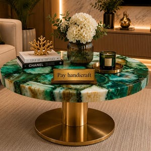 May include: A round coffee table with a green and white agate stone top and a cylindrical gold metal base. On the table are two stacked books, a gold coral sculpture, a glass vase with white flowers, a candle, and a gold sign reading Pay handicraft.