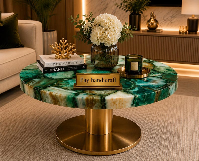 May include: A round coffee table with a green and white agate stone top and a cylindrical gold metal base. On the table are two stacked books, a gold coral sculpture, a glass vase with white flowers, a candle, and a gold sign reading Pay handicraft.