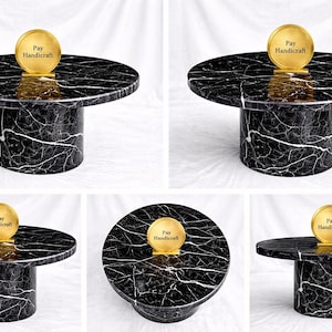 May include: A black and white marble-patterned coffee table with a cylindrical base. The round tabletop supports a gold-colored disc with the text "Pay Handicraft". The table is a modern design.