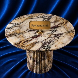 Könnte beinhalten: Ein Tisch mit Marmorplatte und zylindrischem Sockel. Die ovale Tischplatte hat ein goldenes Schild mit der Aufschrift "Pay handicraft". Der Sockel besteht aus vertikalem, strukturiertem Stein. Auf blauem Hintergrund.