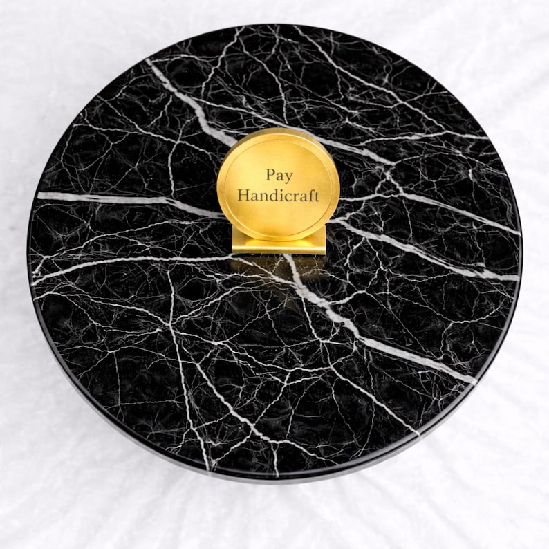 May include: A round, black marble tray with white veining. A gold-colored, circular sign with the text "Pay Handicraft" is centered on the tray. The tray is on a white surface.