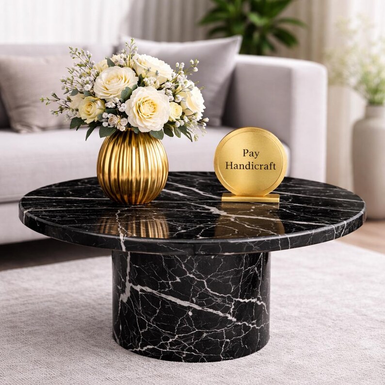 May include: A round black marble coffee table with white veining. A gold vase with white roses and greenery sits on the table. A gold sign with the text "Pay Handicraft" is also on the table.