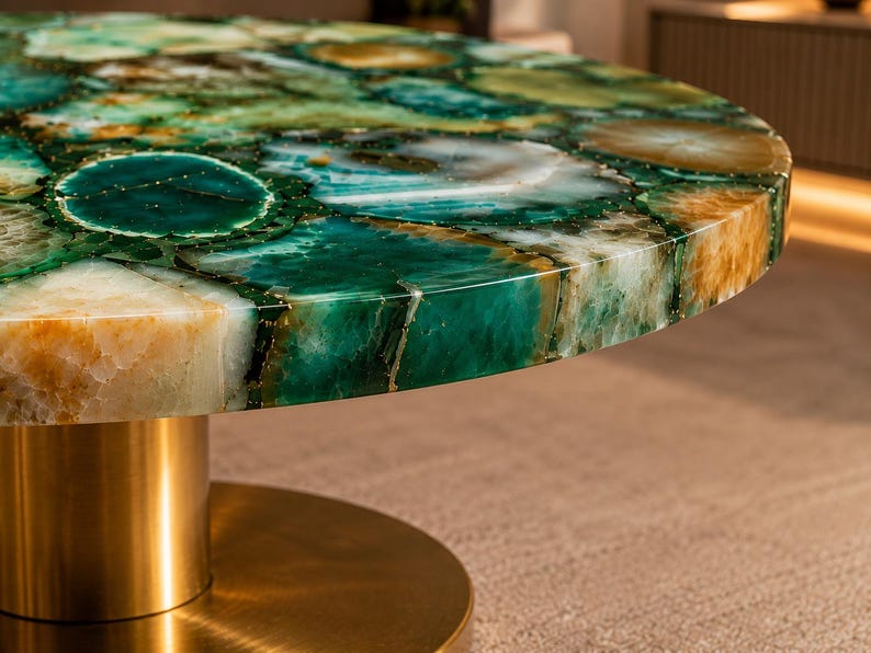 May include: A round coffee table featuring a polished surface made of green and amber agate stone slices with natural crystalline patterns. The tabletop is supported by a cylindrical pedestal base with a smooth, brushed metallic gold finish.