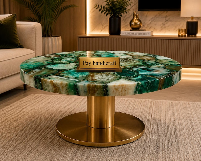 May include: A round coffee table featuring a polished green agate stone top with natural crystalline patterns and a gold-colored metal pedestal base. A small rectangular gold plaque with the text Pay handicraft is placed on the table surface.