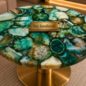 May include: A round table featuring a tabletop composed of numerous polished green and white agate slices arranged in a mosaic pattern. A rectangular brass-colored nameplate with the text Pay handicraft sits on the surface, supported by a gold base.