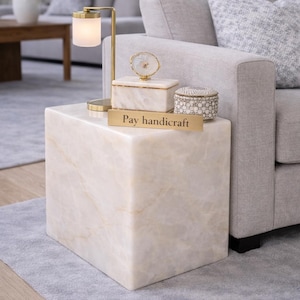 May include: A white ceramic mug with a black handle and the text "But First, Coffee" in a black, bold font. The mug is sitting on a wooden surface. The mug is approximately 4 inches tall.