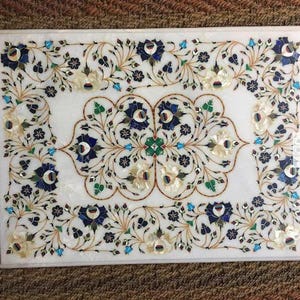 Könnte beinhalten: Ein weißer Marmortischplatte mit aufwendigen floralen Designs, die mit Perlmutt, Blau, Grün und Gold verziert sind.