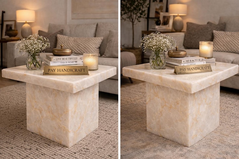 Puede incluir: Una mesa de centro cuadrada de m&aacute;rmol color crema con base de bloque. La mesa est&aacute; adornada con un jarr&oacute;n de flores blancas, libros, una vela y una caja dorada decorativa. Un letrero dorado dice "PAY HANDICRAFT".