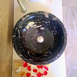 May include: A white ceramic mug with a black handle and the text "But First, Coffee" in a bold, black font. The mug is set against a blurred background, suggesting a cozy setting.